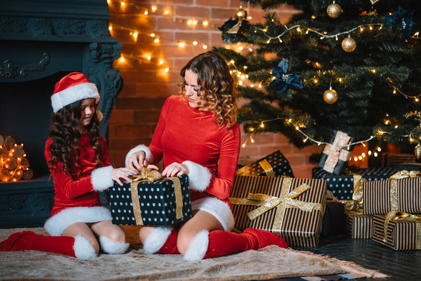 Merry Christmas and Happy Holidays! Cheerful mom and her cute daughter girl in Christmas costumes exchanging gifts. - Fotó, kép