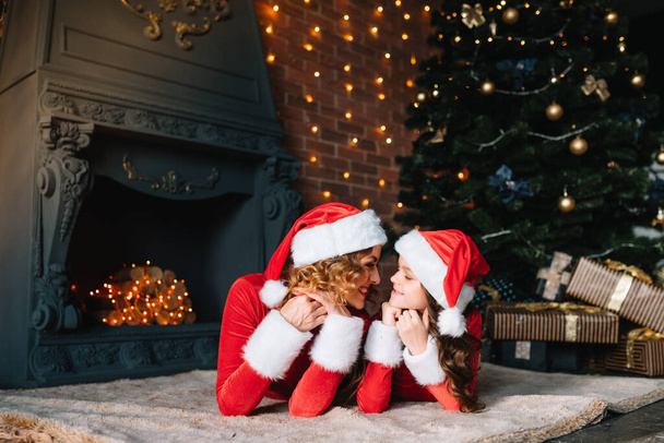 Merry Christmas and Happy Holidays! Beautiful mother with little daughter in Christmas costumes spend time together near the Christmas tree. - Foto, imagen