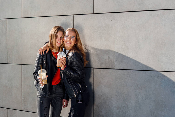 Two beautiful teenage girlfriendss with smoothie posing near grey concrete wall. Leisure time with best friends. - Fotoğraf, Görsel