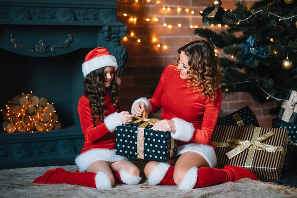 Merry Christmas and Happy Holidays! Cheerful mom and her cute daughter girl in Christmas costumes exchanging gifts. - Fotoğraf, Görsel