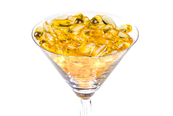 Vaso de vidrio transparente con aceite de pescado cápsulas de gel blando amarillo anaranjado aceite de pescado omega 3 o omega 6, omega 9, vitamina A, vitamina D, vitamina E aislada sobre fondo blanco. Concepto de alimentación saludable - Foto, imagen