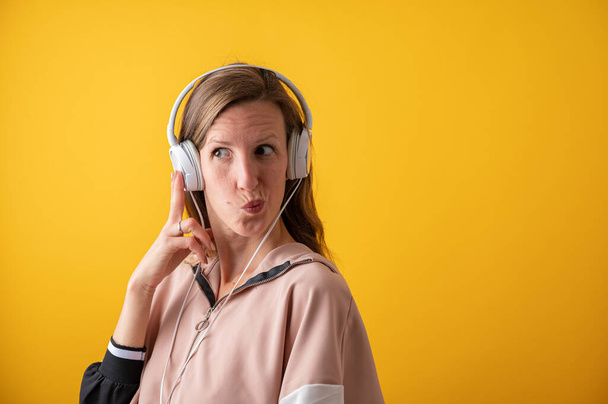 Young woman wearing white headphones making a goofy face. Over bright yellow background. - Foto, imagen