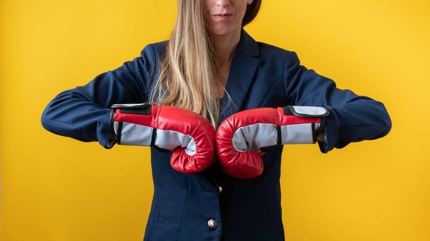 Vooraanzicht van een zakenvrouw met rode bokshandschoenen die vuisten tegen elkaar botst in een conceptueel beeld van machtige vrouwen in het bedrijfsleven. Over gele achtergrond. - Foto, afbeelding