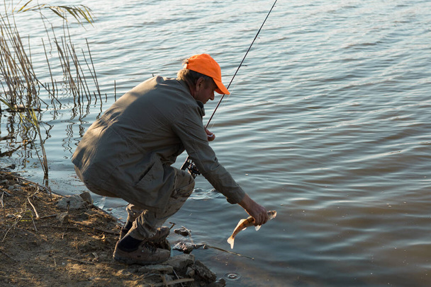 Pescador em pé na margem do rio e tentando pegar um peixe. Desporto, recreação, estilo de vida. - Foto, Imagem