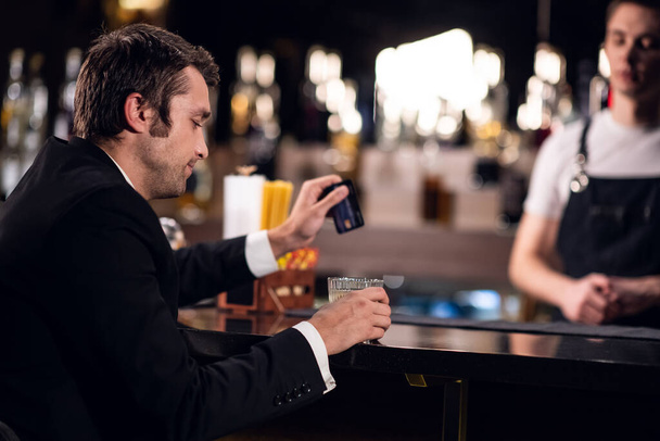 Plastik kart tutan bir adam, barda kokteyl için ödeme yapar. - Fotoğraf, Görsel