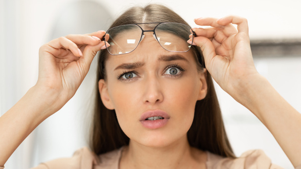 Porträt einer verwirrten jungen Frau, die durch eine Brille blickt - Foto, Bild