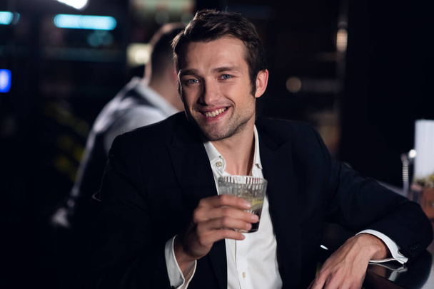 ein schöner Mann posiert für ein Foto an der Bar eines Restaurants mit einem Cocktail in der Hand, Porträt - Foto, Bild
