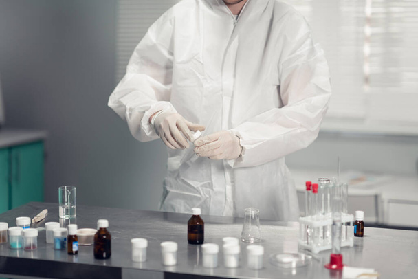 Een close-up van de handen van de wetenschappers met een chemisch monster en een tafel met verschillende laboratoriumglaswaren - Foto, afbeelding