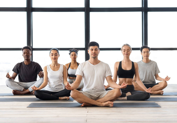 Meditação em grupo. Jovens homens e mulheres multiétnicos meditando juntos na posição de lótus - Foto, Imagem