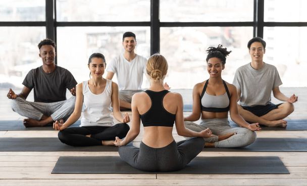 Koncepcja wellness. Kobieta instruktorka jogi mając lekcję grupową z młodymi ludźmi wielorasowymi - Zdjęcie, obraz