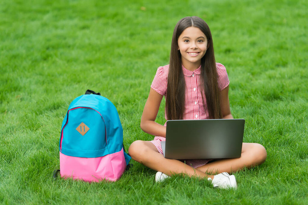 girl reacts while using a laptop sit on green grass in park with school back, education - Foto, Imagem