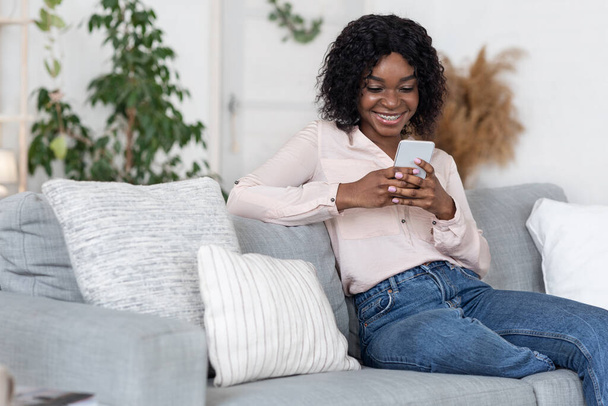 Riposo domestico. felice giovane nero femmina relax su divano con smartphone - Foto, immagini