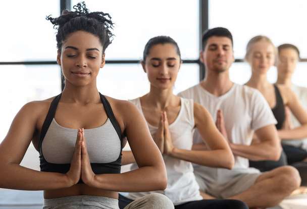 Clase de yoga. Jóvenes deportistas multiculturales sentados en fila, meditando juntos - Foto, Imagen