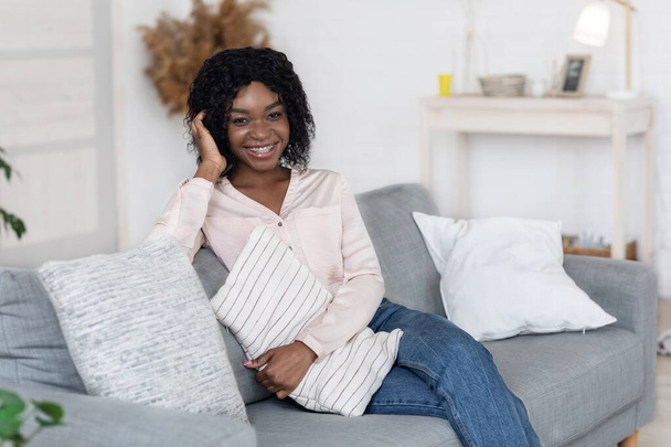 Cozy Weekend. Portrait of cheerful african woman sitting on couch cuddling pillow - Fotoğraf, Görsel