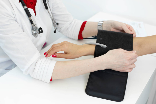Physiotherapist puts on a medical tonometer to measure pressure on the patients arm. - Foto, imagen