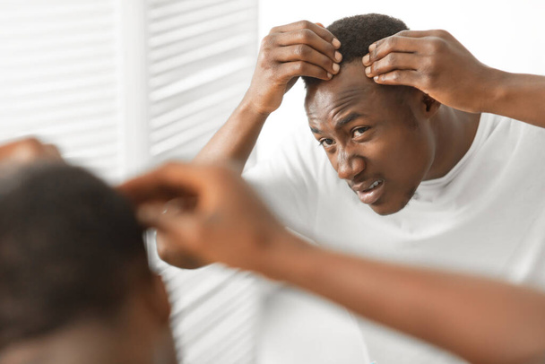 africano hombre tener caspa problema buscando en espejo en cuarto de baño - Foto, Imagen