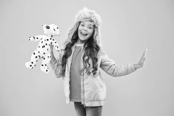 playful beauty. cold season in warm clothes accessory. happy kid pink background. kid fashion. Hipster girl fur winter earflap hat. autumn style. Childhood happiness. little girl dalmatian dog toy - Фото, зображення