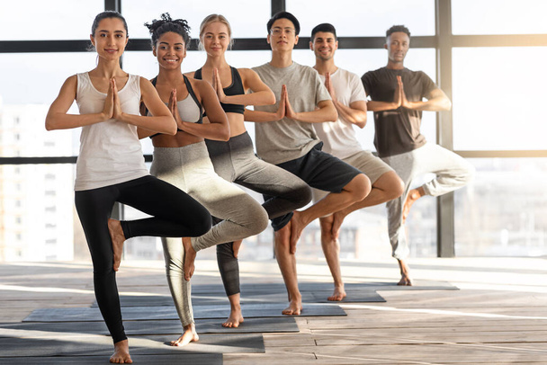 Vrksasana Yoga. Grupo de personas multiétnicas felices practicando la postura del árbol en el estudio - Foto, Imagen