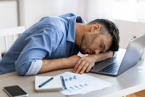 Aludj a munkahelyeden. Kimerült túlhajszolt férfi munkavállalói szundikálás a munkahelyen az irodában - Fotó, kép