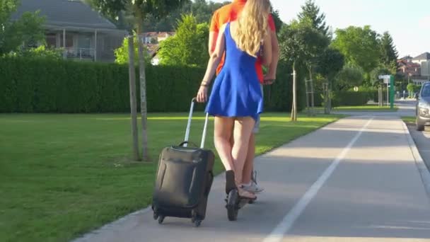 Κοντινό πλάνο: Ζευγάρι βόλτες ένα ηλεκτρικό σκούτερ και σύροντας μια ταξιδιωτική τσάντα πίσω τους - Πλάνα, βίντεο