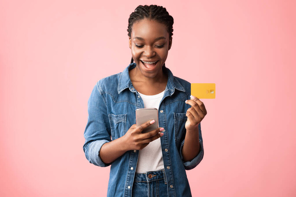 Mujer afroamericana usando Smartphone y tarjeta de crédito, fondo rosa - Foto, imagen