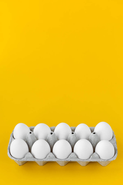 White hen eggs in open cardboard carton on yellow background. Healthy organic food and diet concept. Easter theme. - Foto, Imagem