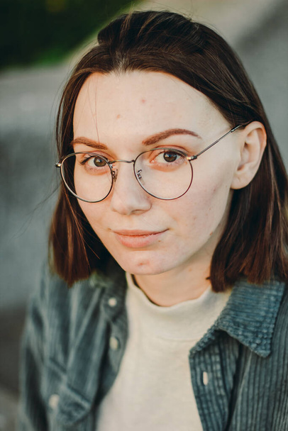 Closeup outdoor portrait of stylish beautiful caucasian young woman with short brunette hair wearing jeans shirt and glasses. Summer sunny evening park at the sunset - Foto, imagen