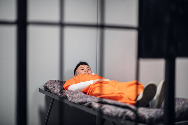 Aasialaisessa korkean turvallisuuden vankilassa oleva vanki makaa punkassa punaisissa vangeissa univormussa eristyssellissä.. - Valokuva, kuva