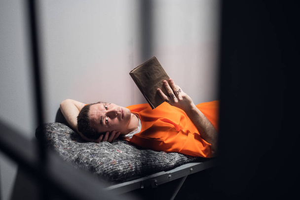 Un peligroso asesino en serie con tatuajes en la cara en una celda lee la Santa Biblia acostada en una litera. - Foto, imagen
