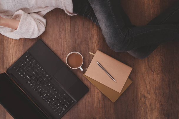 Tasse à café, ordinateur portable, cahiers, crayon, et les femmes allongées sur le sol en bois. - Photo, image