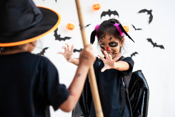 Zwei süße asiatische Kindermädchen in Halloween-Kostümen und Make-up haben gemeinsam Spaß an der Halloween-Feier - Foto, Bild