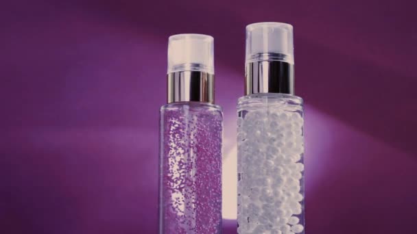 Make-up základna a sérum gel jako luxusní výrobky pro péči o pleť a lesklé světelné erupce na fialovém pozadí, péče o pleť rutina pro kosmetiku obličeje a kosmetické značky - Záběry, video