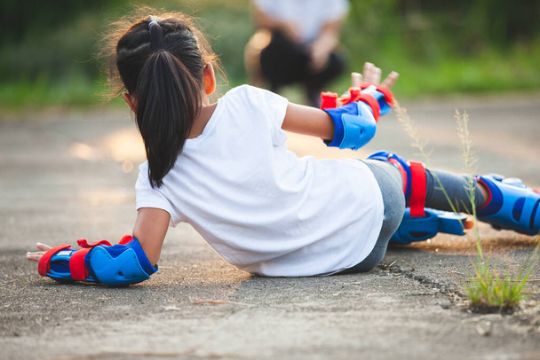 lindo asiático niño chica cabalgando en rodillo patines y caer abajo en el parque - Foto, imagen