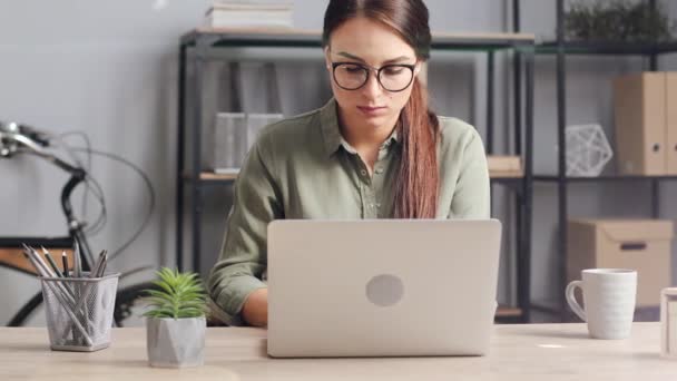 Young beautiful woman with glasses working at home on laptop. Girl is focused on the computer. Freelance concept. - Кадры, видео