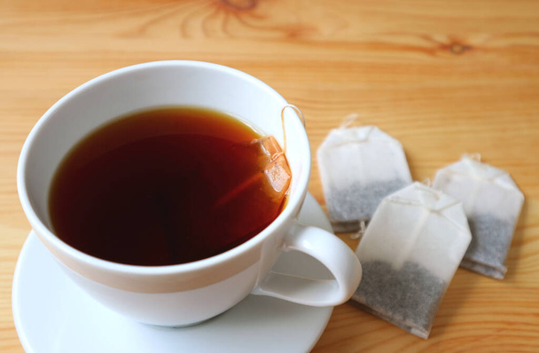 Nahaufnahme heißer Tee in einer weißen Tasse mit verschwommenen Teebeuteln auf einem Holztisch - Foto, Bild
