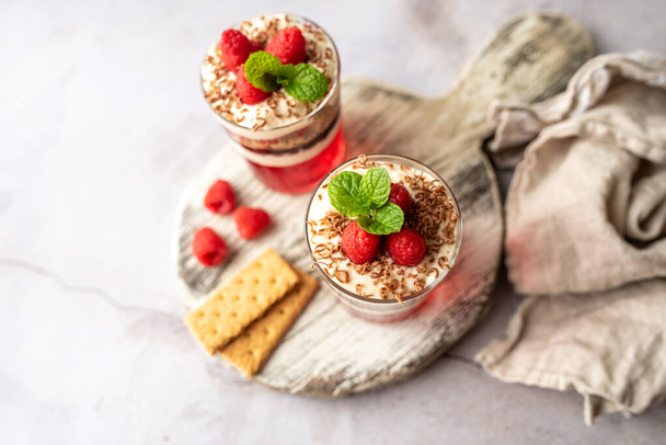 Dessert in a glass cup, with Jello covered in yogurt and topped with fresh raspberries. Mini dessert on light concrete background. Fruit parfait with jello and jelly. - Фото, зображення