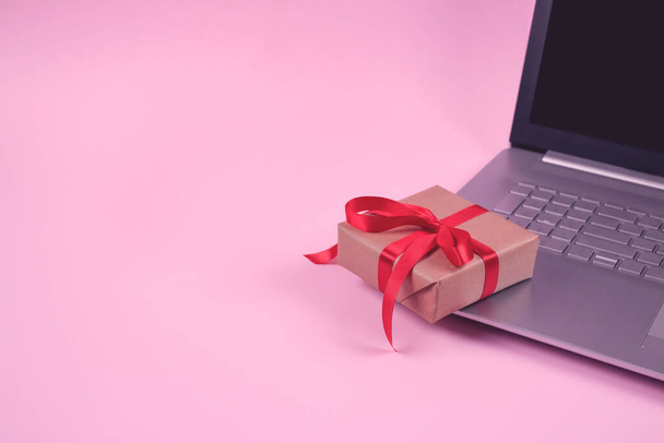Front view on laptop computer and present box with red bow on pastel pink background with copyspace for your text. Seasonal sale, black friday and cyber monday concept. Online shopping - Photo, Image