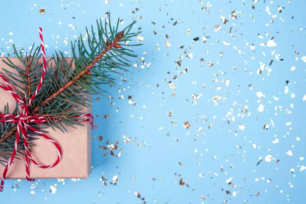 Gift box with red bow and Christmas tree twig on festive blue background with golden sparkles around and copyspace for your text. Flat lay style. Christmas or New Year celebration concept - Photo, Image