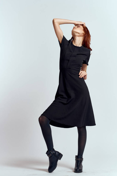 Nainen mustassa mekossa kevyellä taustalla ja sukkahousut kengät punaiset hiukset ja aiheuttavat täyden kasvun - Valokuva, kuva