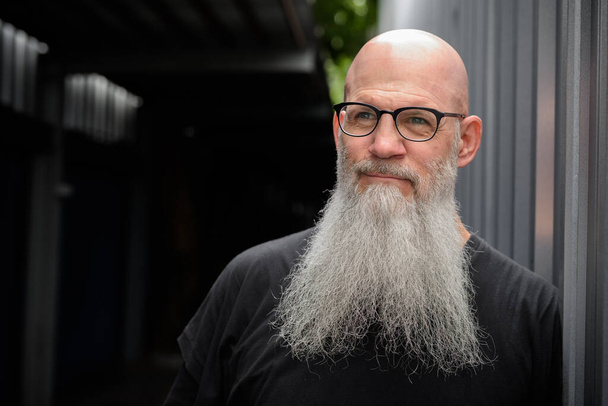 Portrait of mature handsome bald bearded man in the city streets outdoors - Photo, Image