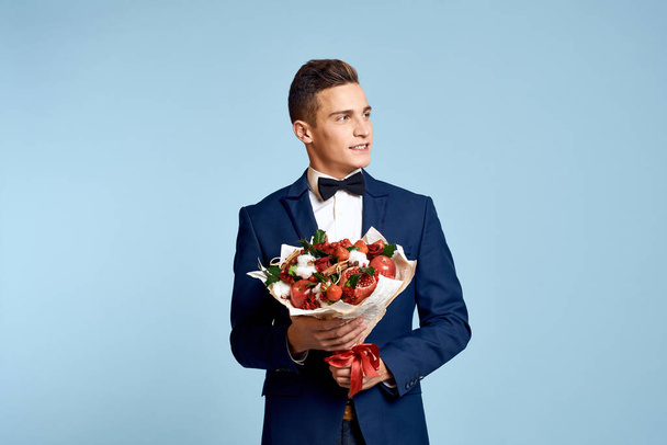 романтичный мужчина с букетом цветов и в галстуке-бабочке на голубом фоне обрезанный вид - Фото, изображение