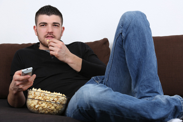 Молода людина дивиться телевізор і їдять попкорн - Фото, зображення