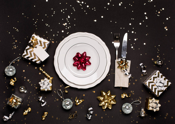 Weihnachten oder Neujahr Tischdekoration mit weißem Teller, Besteck und weihnachtlichem Goldsilber auf schwarzem Hintergrund. Draufsicht, Kopierraum, flache Lage - Foto, Bild