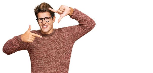 Handsome caucasian man wearing casual sweater and glasses smiling making frame with hands and fingers with happy face. creativity and photography concept.  - Photo, Image