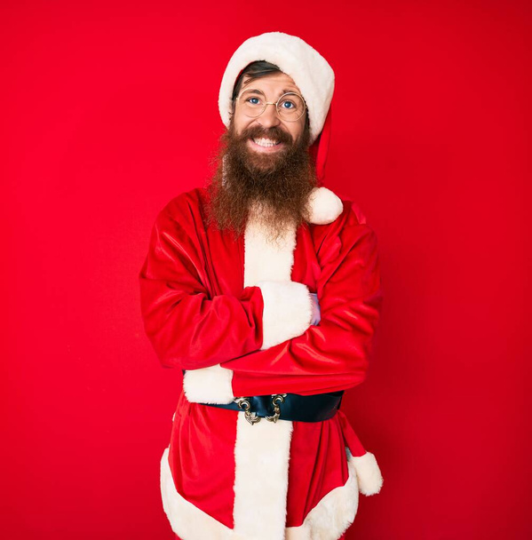 Bonito jovem homem de cabeça vermelha com barba longa vestindo traje de Papai Noel rosto feliz sorrindo com os braços cruzados olhando para a câmera. pessoa positiva.  - Foto, Imagem