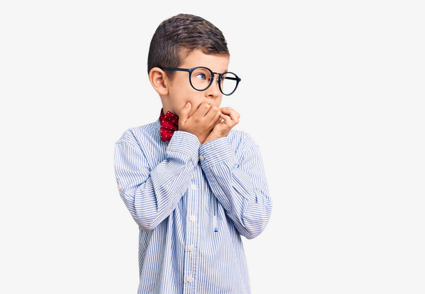 Cute blond kid wearing nerd bow tie and glasses looking stressed and nervous with hands on mouth biting nails. anxiety problem.  - Photo, Image
