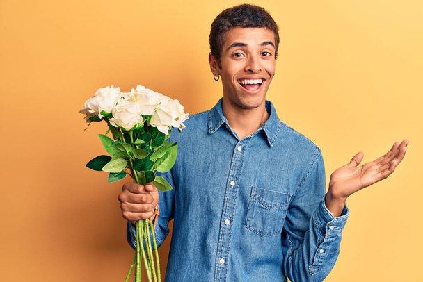 Young african amercian man holding flowers celebrating achievement with happy smile and winner expression with raised hand  - Fotografie, Obrázek