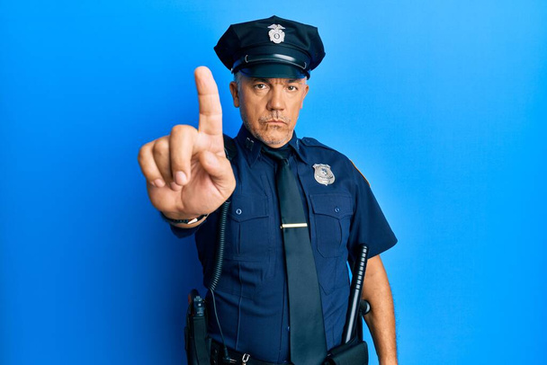 Knappe middelbare leeftijd volwassen man dragen politie-uniform wijzen met de vinger omhoog en boze uitdrukking, tonen geen gebaar  - Foto, afbeelding