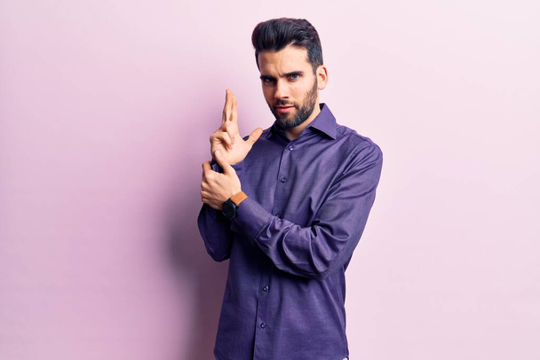 Young handsome man with beard wearing casual shirt holding symbolic gun with hand gesture, playing killing shooting weapons, angry face  - Fotó, kép
