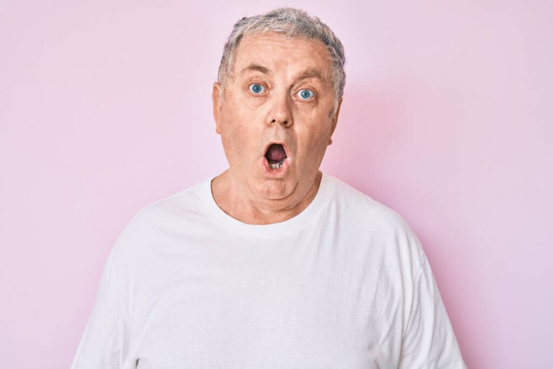 Senior grey-haired man wearing casual white tshirt scared and amazed with open mouth for surprise, disbelief face  - Photo, Image